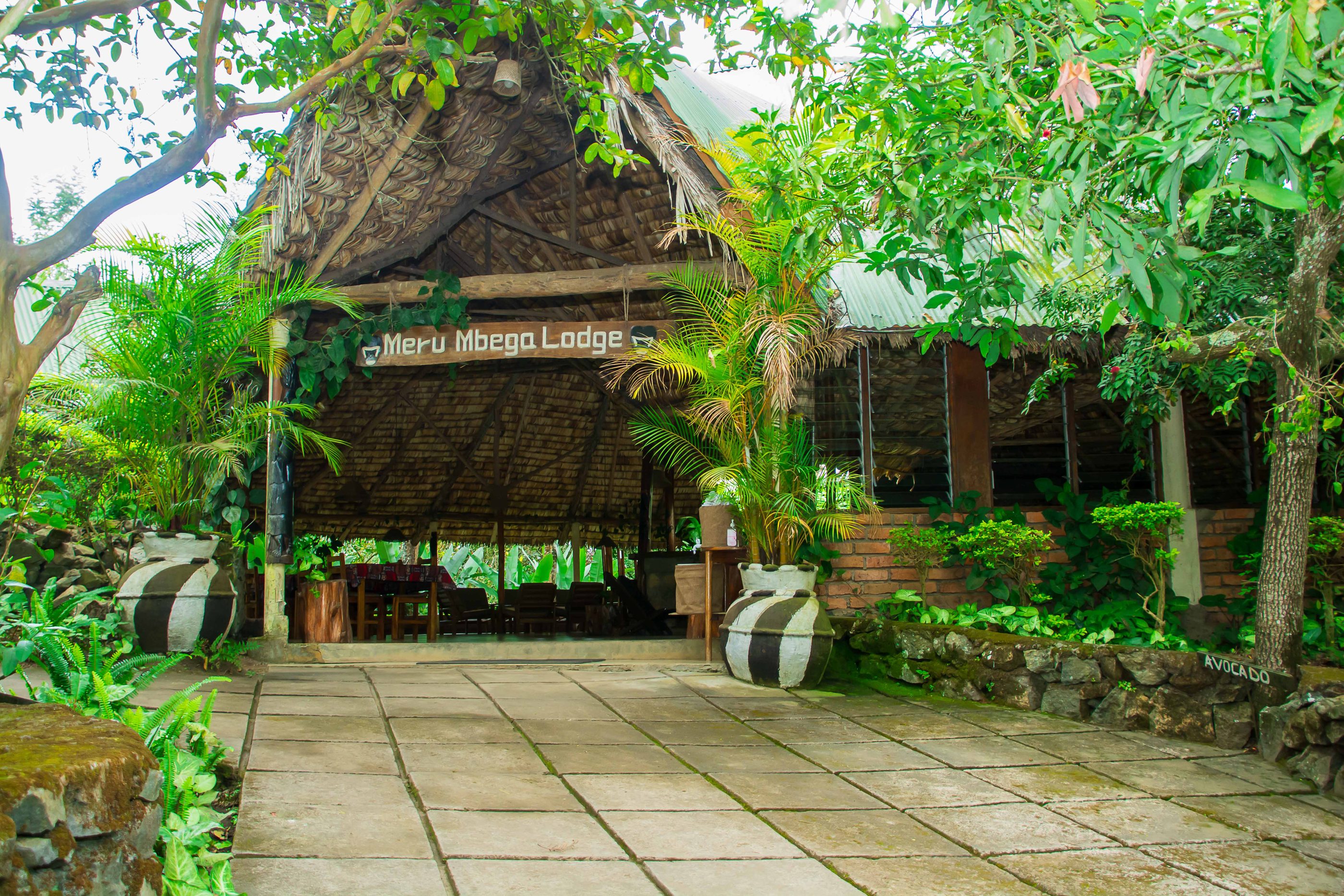 The thatched main building of Meru Mbega Lodge among tropical gardens