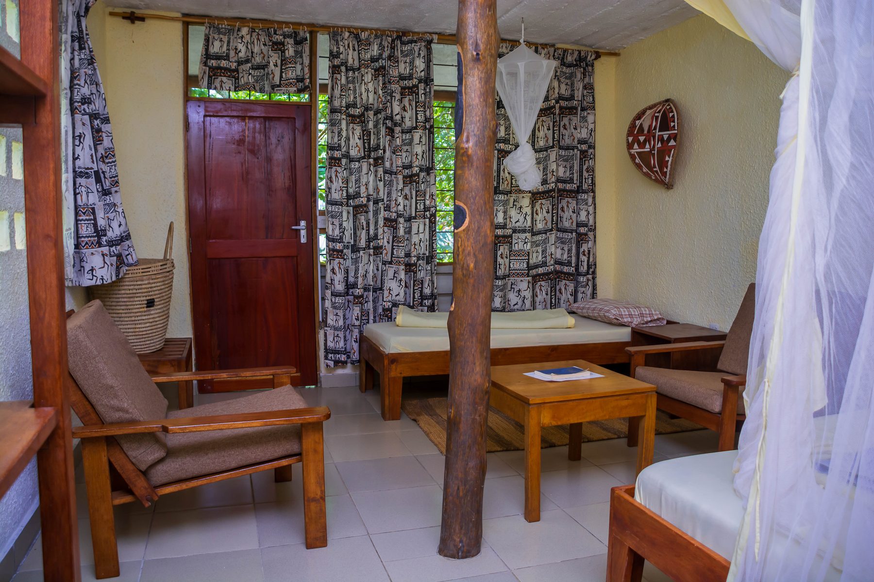 Inside a lodge room: timber chairs, a day bed and a mosquito net over the bed